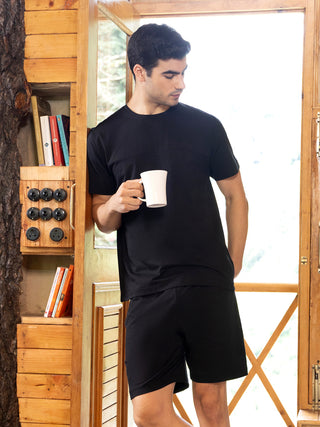 Men in a black crew neck t-shirt and black shorts, holding a white mug.