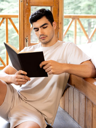 Men wearing light beige loungewear shorts and t-shirt while reading a book.