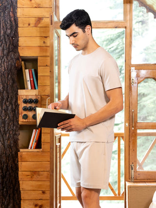 Men, a model wearing a light beige t-shirt and shorts set, standing and reading a book.