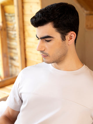 A man in a light grey t-shirt rests his head against a wooden backdrop.