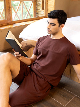 A man in a maroon t-shirt and shorts reads a book.