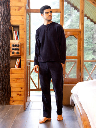A man stands wearing dark navy plush sleepwear consisting of a long-sleeved top and pants.