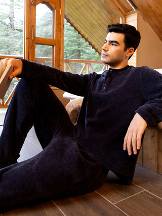 A man in dark blue velvet loungewear poses looking out a window.