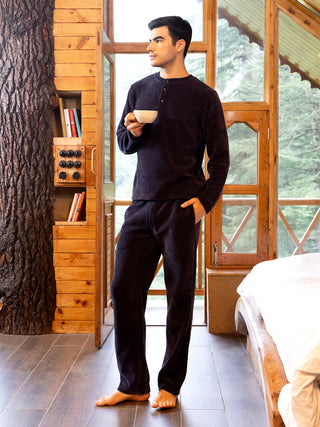 Men in a dark blue, solid-colored terry knit pajama set, standing with a cup of coffee by a window.