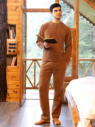 A man in a brown loungewear set with a book in hand.