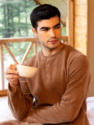 Men in a brown henley pajama top holding a mug.