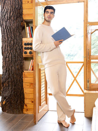 Men are wearing a cream-colored lounge set, the top is a crew neck sweater and the bottom is comfortable lounge pants, in a relaxed pose while reading a book.