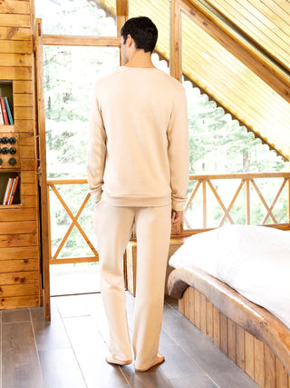 A man stands facing away from the camera, wearing a beige pajama set.