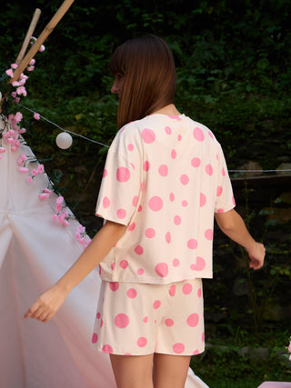 A woman models a light pink polka dot pajama set with a loose-fitting top and shorts, while facing away from the camera.
