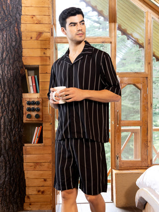 Men in a vertical striped black sleepwear set, holding a white mug, standing in a cabin.