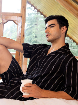 Men lounging in black striped pajamas holding a white mug, with the garment featuring a revere collar and relaxed fit.