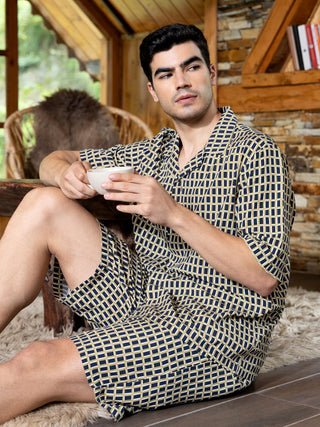 Men wearing a navy and yellow patterned pajama set, sitting down with a mug.