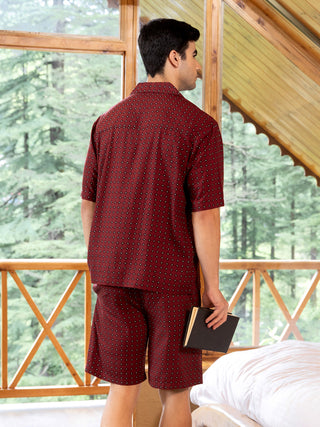 Men's maroon printed sleepwear set, standing and holding a book.
