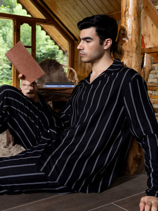 A man in black and white striped pajamas is sitting and reading a book.