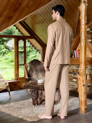 A man models beige pajamas with a small geometric print in a cozy cabin setting.