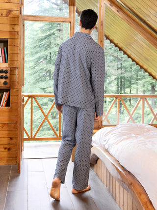 A man wearing blue printed pajamas walks into a room with a wooden interior and large windows overlooking a forest.