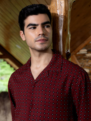 Men in a patterned burgundy sleep shirt, leaning against a wooden beam.