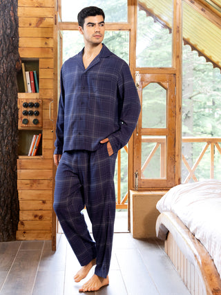 A man in a blue plaid pajama set stands with his hand in his pocket.