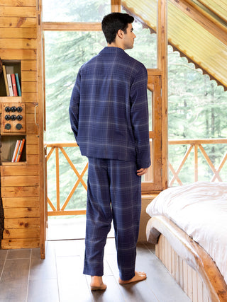Men's navy blue plaid pajama set, standing and looking out a window.