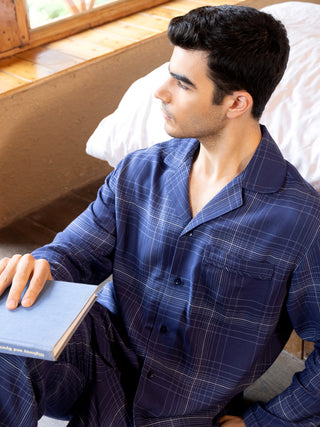 Men in navy blue plaid pajamas sitting on the floor holding a book.