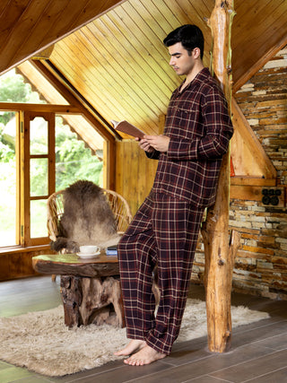Men in a burgundy plaid pajama set lounging by a rustic wooden pillar.