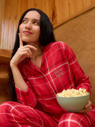 A woman in red plaid Tom and Jerry pajamas, sitting with a bowl of popcorn, looks thoughtfully to the side.