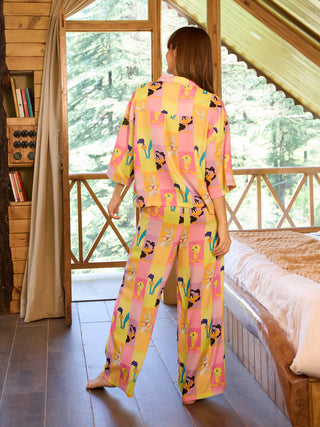 Women posing from behind in a yellow and pink checkered sleepwear set featuring a Bugs Bunny print, with a bed and window in the background.