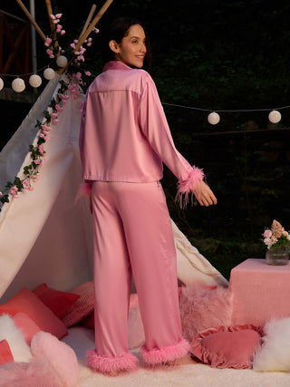 A woman is posing wearing pink feather-trimmed satin pajamas.
