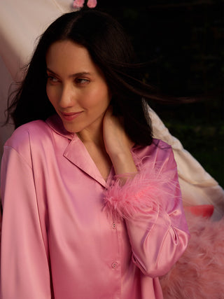 A woman in a pink satin pajama set with feather trim.