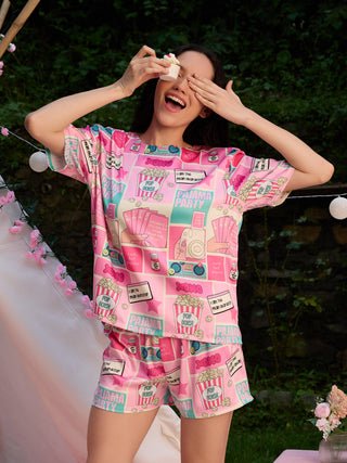 A woman in a pink pajama set with a "Pajama Party" print holds a cupcake to her eye.