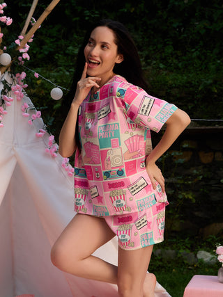 A woman poses playfully in pink pajama set featuring a "Pajama Party" print with popcorn and comic book style elements.