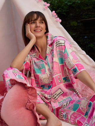 A woman in a pink pajama set with a comic book-style print featuring "Pajama Party" and "Pop Corn" slogans, strikes a relaxed pose.