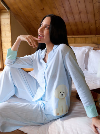 A woman in blue and white striped pajamas with a French bulldog print is sitting on a bed.