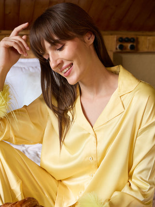 Women wearing yellow satin pajamas with feather trim, sitting on a bed.
