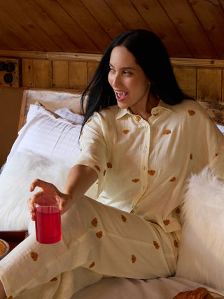 A woman poses in light yellow, bear-printed sleepwear, holding a glass of pink drink.