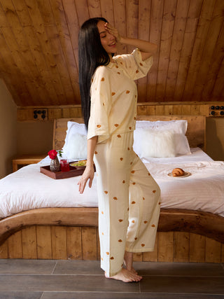 A woman models a light yellow pajama set with a heart print, standing with her hand over her eyes.
