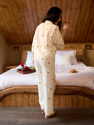 A woman poses wearing a cream pajama set with a teddy bear print, holding a drink.