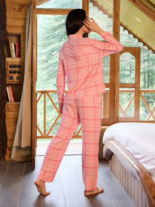 Women in a pink plaid pajama set, standing with their back to the camera, looking out a window.