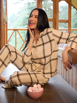 A woman in cream and black plaid pajamas sits on the floor next to a bowl of marshmallows.