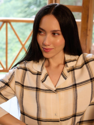 A young woman with long, dark hair is wearing a cream-colored plaid pajama set.