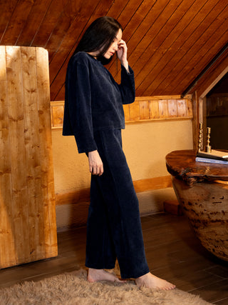 Women in a navy blue velvet pajama set, standing with their hand on their forehead, and the other hand resting on their hip.