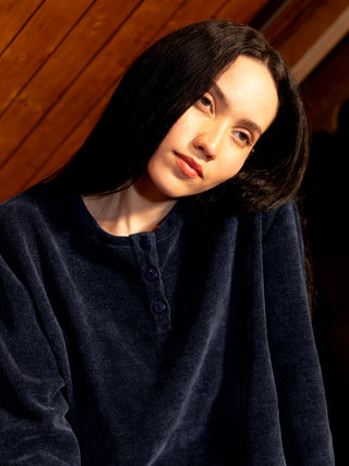 A woman in a navy blue velvet henley sleep shirt.