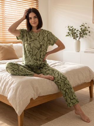 A woman in a green printed pajama set poses on a bed.