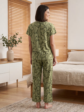 Women's olive green pajamas with a swirling abstract print, standing.