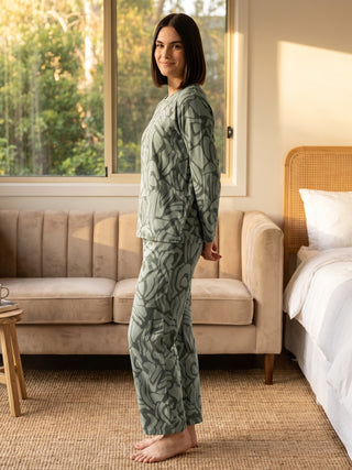 A woman poses sideways in green printed pajamas.