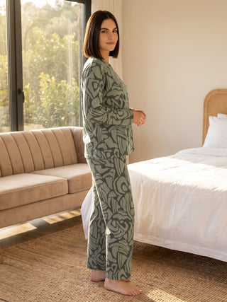 A woman is standing in a bedroom wearing green pajamas with a abstract print.