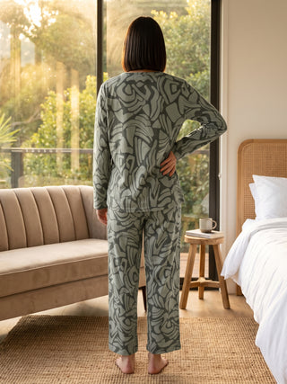 Women in pajamas with a gray-green abstract print, standing with their back to the camera, looking out a window.