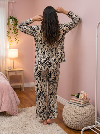 Woman in a black and cream patterned pajama set, standing with her back to the camera, arms raised.