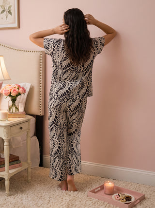 Woman in black and white patterned pajamas stands with hands behind her head.