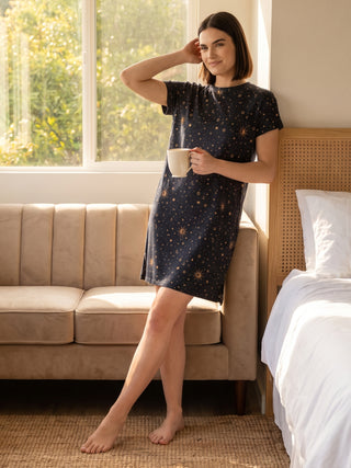 Women in a dark navy, short-sleeved sleep dress with a celestial print, holding a mug.